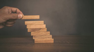Yakın plan el, çöküşü veya finansal risk yönetimi ve stratejik planlama kavramlarını önlemek için piramit şeklinde dizilmiş ahşap blok kulesini ihtiyatlı bir şekilde yerleştiriyor.