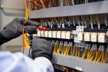 Elektrik mühendisinin ölçüm ekipmanlarını kullanarak devre kesici ve kablo tesisat sistemindeki elektrik akımını kontrol ederek ana güç dağıtım panosunun bakımı için yakın çekim eli..