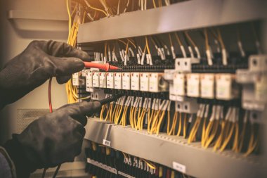 Elektrik mühendisinin ölçüm ekipmanlarını kullanarak devre kesici ve kablo tesisat sistemindeki elektrik akımını kontrol ederek ana güç dağıtım panosunun bakımı için yakın çekim eli..