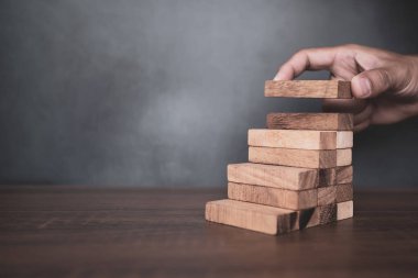Yakın plan el, çöküşü veya finansal risk yönetimi ve stratejik planlama kavramlarını önlemek için piramit şeklinde dizilmiş ahşap blok kulesini ihtiyatlı bir şekilde yerleştiriyor.