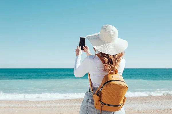 Kobieta Używająca Smartfona Kapeluszu Żółtym Plecaku Plaży — Zdjęcie stockowe