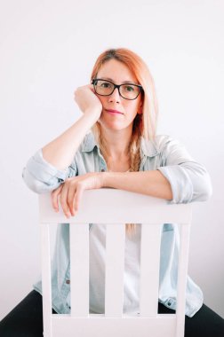 Evde sandalyede oturan, gözlüklü, sıkkın bir kadın.