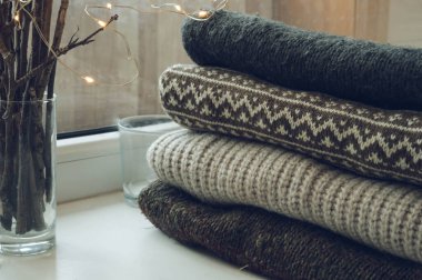 Beyaz pervaza örülmüş bir kazak yığını. Camdaki dallar. Lider ışıklar. Hygge sıcak kavramı.
