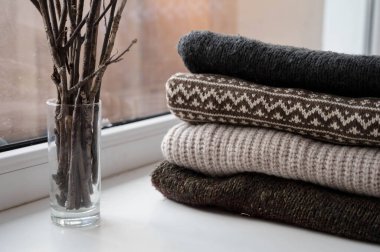 Beyaz pervaza örülmüş bir kazak yığını. Camdaki dallar. Lider ışıklar. Hygge sıcak kavramı.