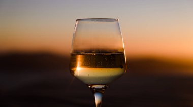 Şampanyalı şampanyayla yakın plan. Arkaplanda gün batımı gökyüzü.