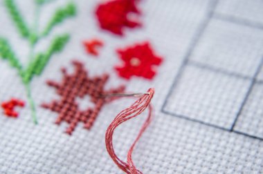 Çapraz dikişe yakın çekim. İpliği olan bir iğne tuvale sıkıştı. Bir parça nakış.