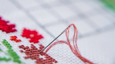 Çapraz dikişe yakın çekim. İpliği olan bir iğne tuvale sıkıştı. Bir parça nakış.