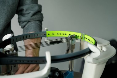 Elektronik telli makinede tenis raketinin yakın çekimi. Oyundan önce sentetik bağırsak teli değiştirme işlemi. Gazetecinin elleri.
