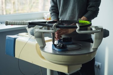 Elektronik telli makinede tenis raketinin yakın çekimi. Oyundan önce sentetik bağırsak teli değiştirme işlemi. Gazetecinin elleri.
