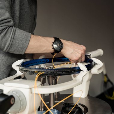 Elektronik telli makinede tenis raketinin yakın çekimi. Oyundan önce sentetik bağırsak teli değiştirme işlemi. Gazetecinin elleri.