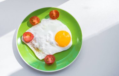 Taze pişmiş yumurta ve ikiye bölünmüş kiraz domatesleri yeşil bir tabakta yatıyor. Sağlıklı kahvaltı. Yakın plan. Yukarıdan görüntüle.