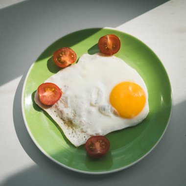 Taze pişmiş yumurta ve ikiye bölünmüş kiraz domatesleri yeşil bir tabakta yatıyor. Sağlıklı kahvaltı. Yakın plan. Yukarıdan görüntüle.