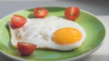 Taze pişmiş yumurta ve ikiye bölünmüş kiraz domatesleri yeşil bir tabakta yatıyor. Sağlıklı kahvaltı. Yakın plan..