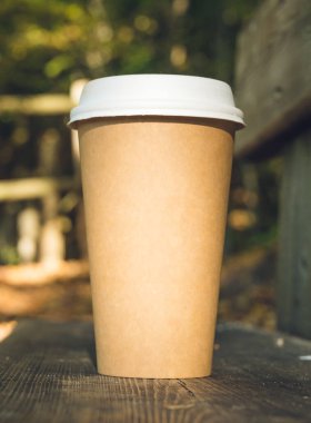 Sonbahar ormanında bankta duran küçük bir karton kahve fincanı. Düşen yapraklar. Yakın plan. Sıcak içecek..