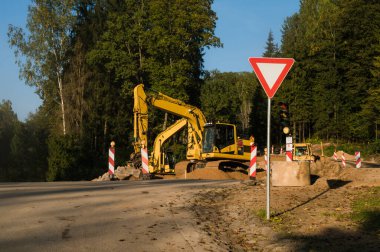 Yeni bir yol inşa etme süreci. Sarı kazıcılar. Ağır ekipman. Yol işareti ver..