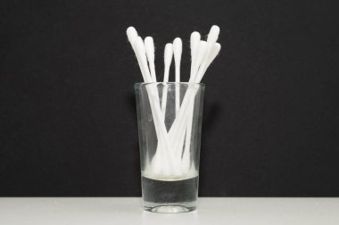 Cam bardaktaki pamuklu çubukları yakından çek. Siyah arkaplan.