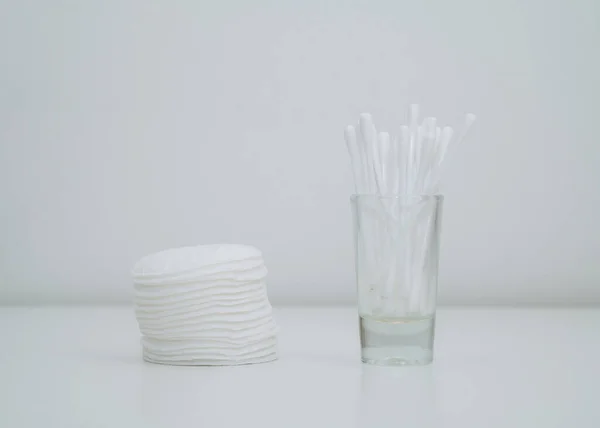 Close-up of stack of cotton pads and cotton swabs in a glass cup. White background.