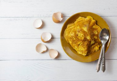 Üst manzara Tayland omleti ya da kaşık ile kavrulmuş seramik tabakta kızarmış yumurta. Beyaz masadaki yumurta kabuğunun yanında. Tayland sokak yemeği. Geleneksel Tayland usulü yemek. Ev yapımı yemek..