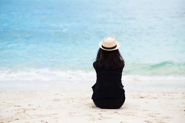 Asyalı Tenli Siyah Tişörtlü Hasır Şapkalı Bir Kadın Kumsalda Oturuyor — Stok fotoğraf