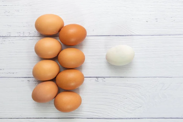 white egg with front many egg on white table wooden background. chicken egg inside duck egg or Different human in the social or different business concept. Selective focus. Life of Alone concept.