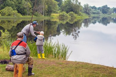 Balık tutmaya. Baba, oğul, büyükbaba, gölün sakin sularında balık tutan oltalarla yaz manzarası. Orman Gölü. Doğal arka plan. Uzayı kopyala Yaşam tarzı. Rahatla.