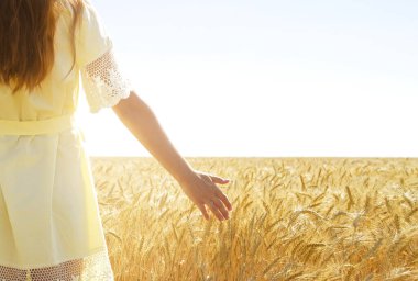 Kız elini tarlada olgunlaşmış buğdayın kulaklarının üzerinden geçiriyor. Boşluğu kopyala.