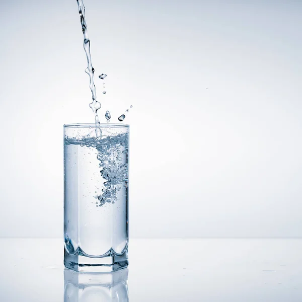 Fresh water pouring into glass on blue background with copy space