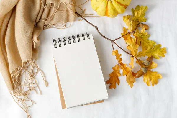 Autumn Thanksgiving card. Open notepad, cashmere scarf and fallen acorn leaves on white linen background.