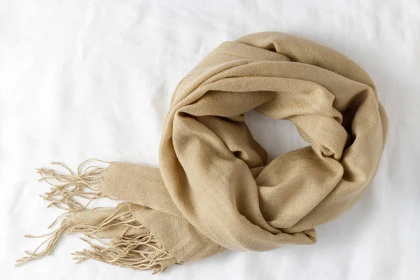 Beige classic soft scarf made of fine pure cashmere with tassels on a white linen background