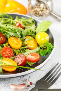 Çeri domatesli, zeytinyağlı ve baharatlı vejetaryen taze roka salatası. Tabak beyaz taş arka planda