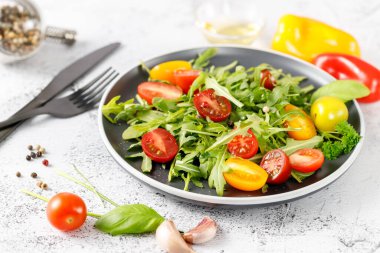 Çeri domatesli, zeytinyağlı ve baharatlı vejetaryen taze roka salatası. Tabak beyaz taş arka planda