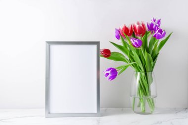 Cam vazoda çiçek açan kırmızı mor lale çiçekleri ve boş poster ya da iç taraftaki beyaz mermer masada fotoğraf çerçevesi modeli. Kopyalama alanı olan hafif arkaplan. 