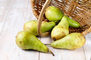 Taze yeşil armut konferansı ahşap masaya hasır sepetten düşüyor. 