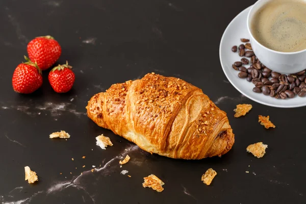 Fresh baked butter nougat crushed nuts breakfast croissant, coffee cup with beans  and crumbs   on dark marble table