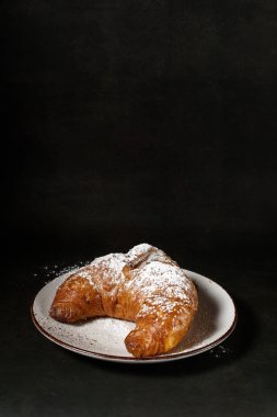 Taze tereyağlı kruvasan, beyaz seramik tabakta şeker tozu ve klasik kahverengi arka plan. Fotokopi alanı olan fırın ya da pastane kartı