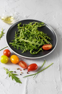 Çeri domatesli taze vejetaryen roka salatası, zeytinyağı ve koyu tabakta baharatlar. Beyaz taş zemin üzerinde üst görünüm çanağı