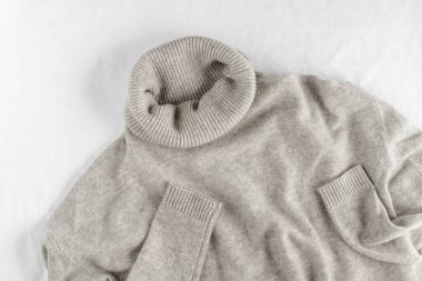 Beyaz keten arka planda uzanan açık gri, lüks, doğal kaşmirden yumuşak bir kazak. Sonbahar ve kış saf yün giysiler.