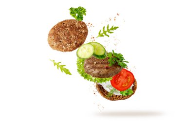 Izgara sığır pirzolası, taze otlar ve beyaz arka planda uçuşan sebzeli sandviç tostu. Biftek köftesi malzemesi dökülüyor.