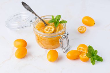 Tatlı kumkatlı reçel ya da cam kavanozda marmelat kaşıkla taze çiğ bütün ve beyaz mermer masa arkasında nane yapraklı kesilmiş meyveler. Egzotik tropikal kimyon meyvesi.