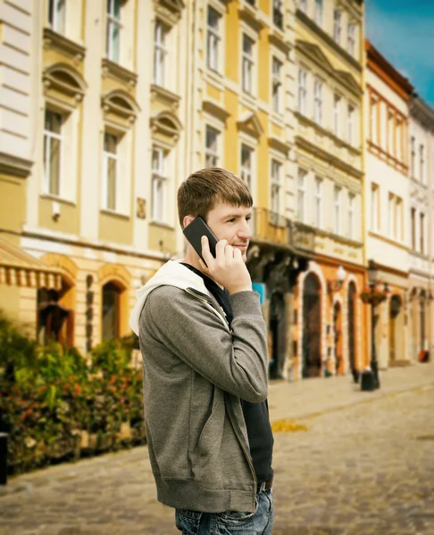 Ung man talar via telefon på gatan Stockfoto