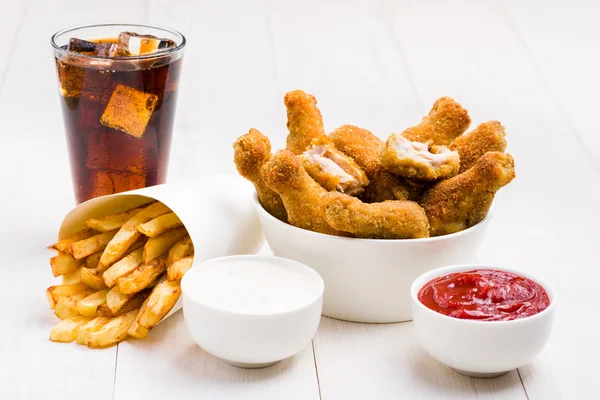 Asas de frango, batatas fritas, coca-cola e molhos na mesa — Fotografia de Stock