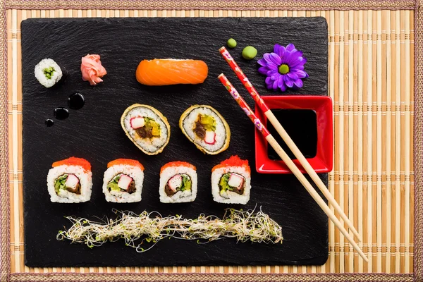 Sushi na placa de pedra preta em uma vista superior de esteira de bambu — Fotografia de Stock