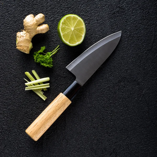 Knife and food ingredients on black stone table top view — Stock Photo, Image