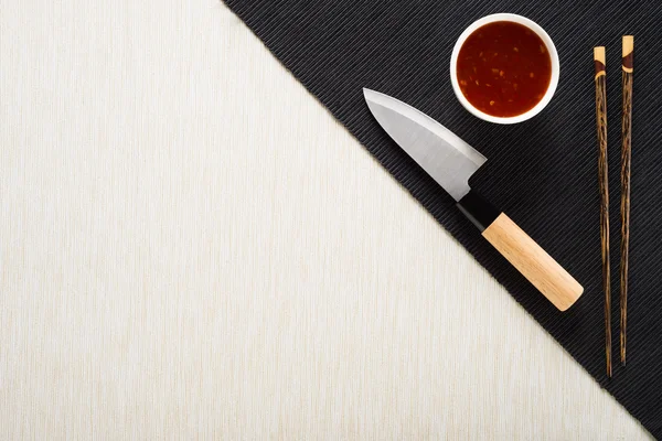 Chopsticks, faca e tigela com molho no tapete de mesa vista superior — Fotografia de Stock