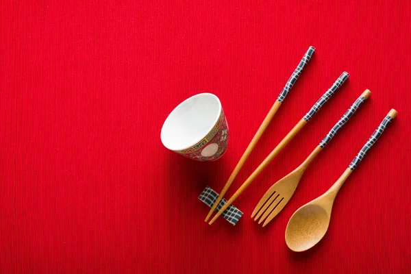 Китайская миска, вилка, ложка и палочки для еды на красном коврике вид сверху — стоковое фото