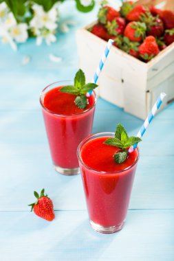 Strawberry smoothie and flower petals on blue background