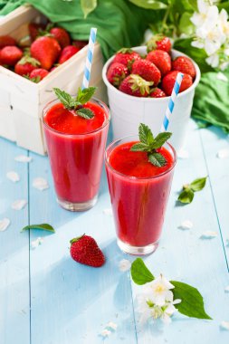 Strawberry smoothie and flower petals on blue background