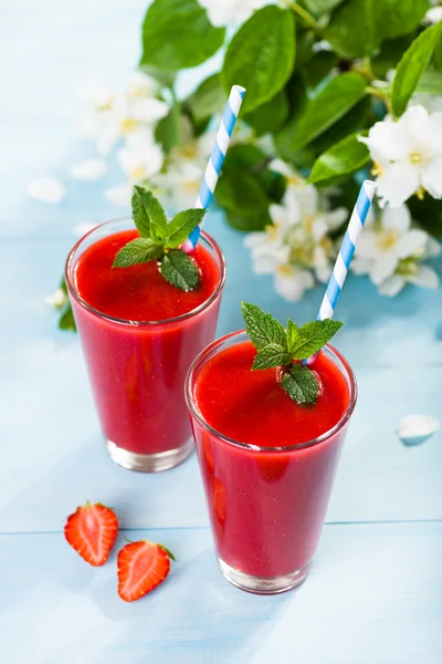 Strawberry smoothie and flower petals on blue background 免版税图库照片