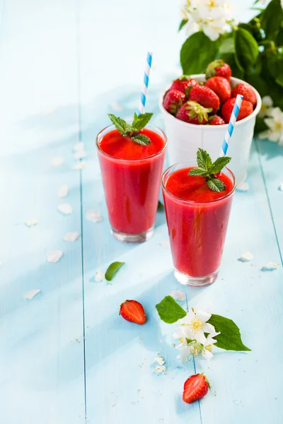 Strawberry smoothie and flower petals on blue background 免版税图库图片