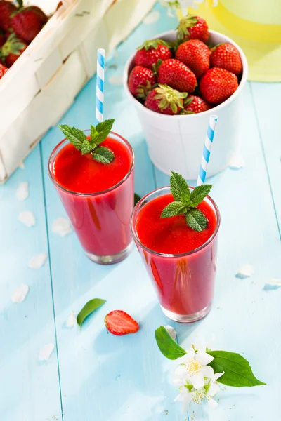 Strawberry smoothie and flower petals on blue background 图库图片